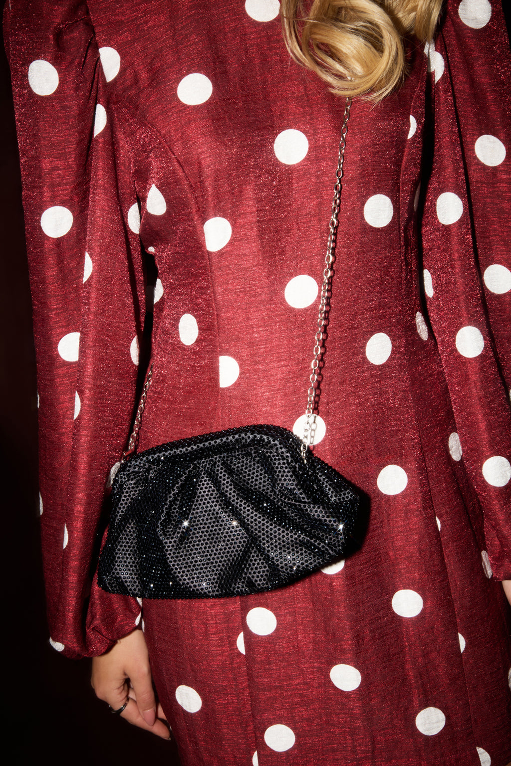 Person wearing a red polka dot dress holding a black handbag.