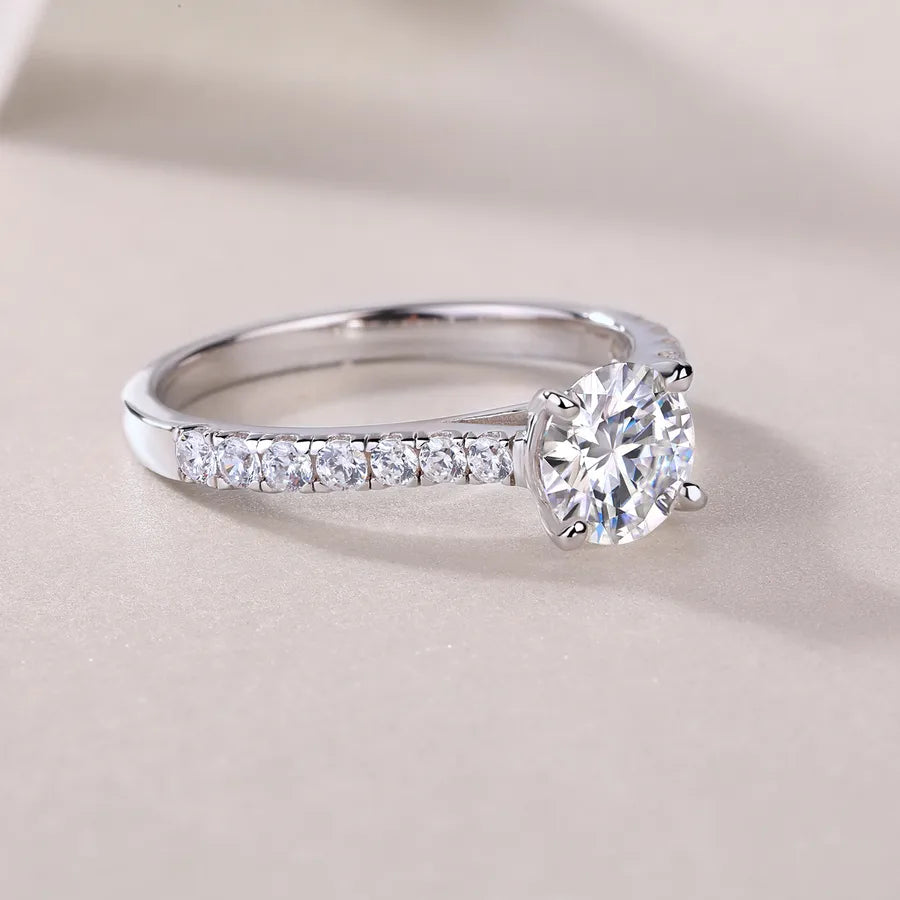 Silver ring with a large diamond and smaller diamonds on the band against a beige background
